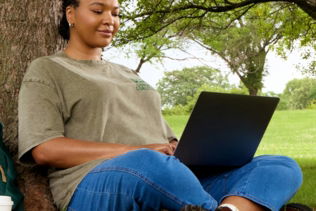 Woman using laptop while sitting under a tree
